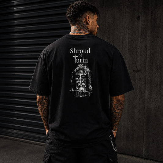 Oversized black Christian streetwear t-shirt featuring distressed Shroud of Turin back graphic worn by tattooed male model in luxury urban environment